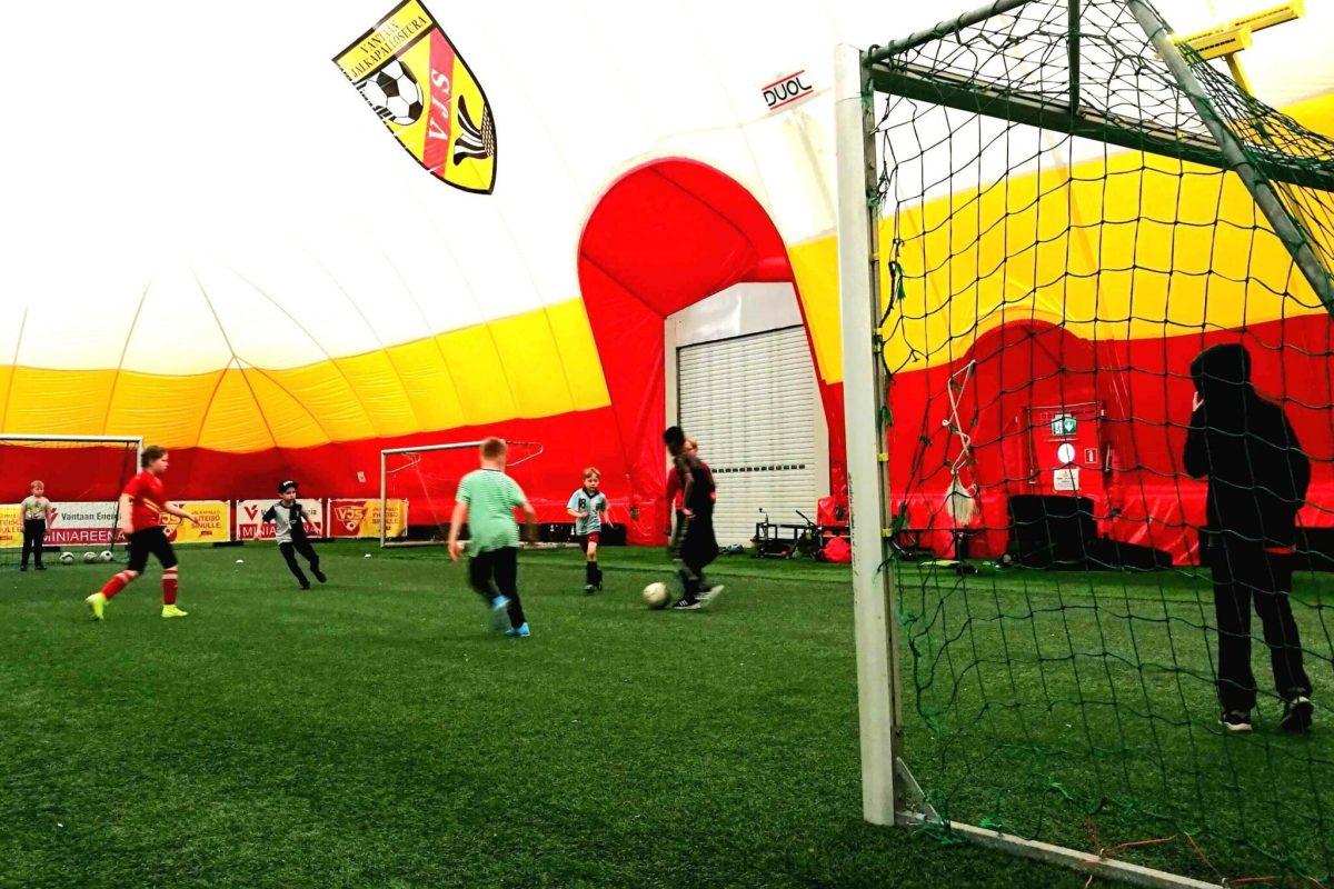 lapsia pelaamassa jalkapalloa jalkapallohallissa.